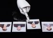 Robotic hand with extended finger points at a row of four Polaroid photos of businesspeople on a dark surface.
